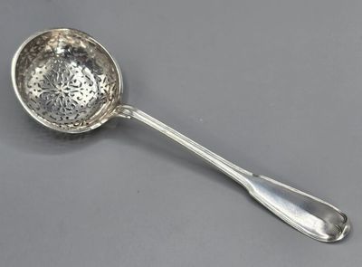une cuillère en argent avec un manche, posée sur une surface grise
