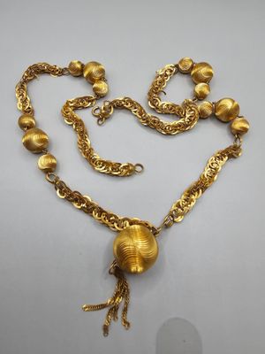 un collier en or orné d'une boule et d'une chaîne, posé sur un fond blanc