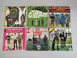 six pochettes d'albums des Beatles posées sur une table, avec une horloge en arrière-plan
