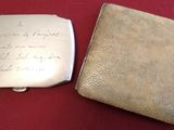 two silver cigarette cases with writing on them sitting on a red surface
