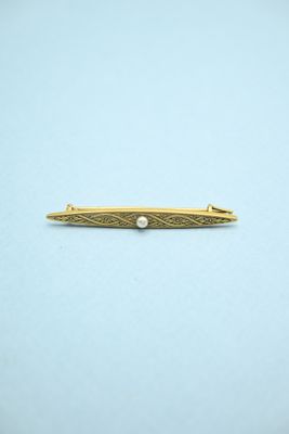 a gold tie bar with a pearl in the center