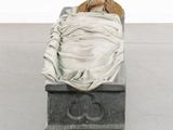 statue of a woman wrapped in a blanket sitting on a box