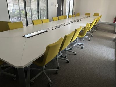 une longue table avec des chaises jaunes et un ordinateur portable posé dessus