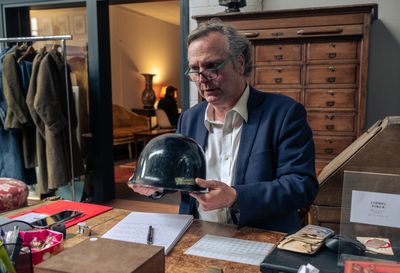 un homme assis à un bureau, tenant une clochette à la main
