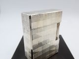 a silver box on a black surface with a clock in the background