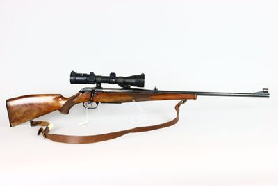 the rifle is laying on a white surface with a scope on it