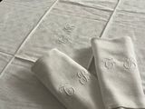 trois serviettes de table en lin blanc ornées de monogrammes, posées sur une table