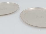 two silver plate with initials on them sitting on a white surface
