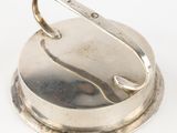 an antique silver plate with a hook on it on a white surface