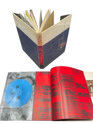un livre ouvert posé sur une surface blanche, à côté d'un disque bleu