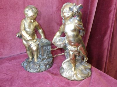pair of antique bronze figurines of cherensils on a pink background
