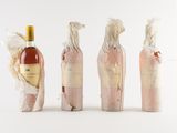 four bottles of wine wrapped in plastic wrappers with a bottle of wine in the background