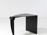 une table noire au plateau incurvé, posée sur un socle blanc