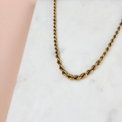 un gros plan d'un collier à chaîne en or posé sur une surface en marbre