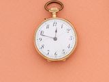 une montre de poche en or posée sur une surface couleur pêche