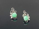 une paire de boucles d'oreilles en jade vert et diamants posées sur un fond noir