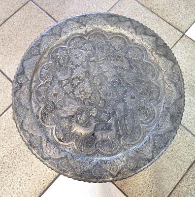 une assiette en argent ornée d'un motif, posée sur un sol carrelé