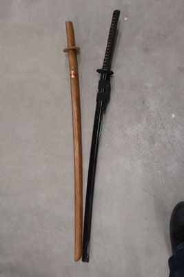 Une personne se tient à côté d'une paire de chaussures noires et d'un bâton en bois.