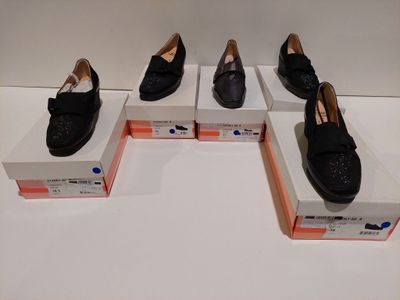 Quatre paires de chaussures noires sont exposées dans une vitrine.