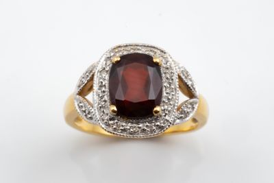a close up of a ring with a garnet stone surrounded by diamonds