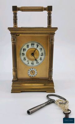 une petite horloge dorée avec une clé, sur fond blanc
