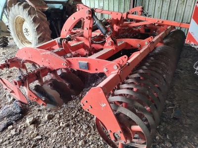 une charrue rouge posée dans la terre à côté d'un tracteur