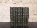six green books are lined up on a black table