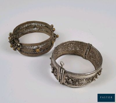 une paire de bracelets en argent posés sur une surface blanche avec un fond bleu