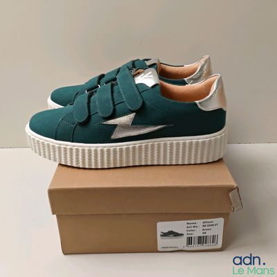des baskets vertes et argentées à semelle blanche, posées sur une boîte en carton