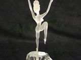 une sculpture blanche représentant une femme debout sur un rocher, les bras tendus