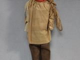 une image représentant une poupée vêtue d'habits marron et de bottes, sur fond blanc