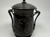 un vase noir muni d'un couvercle, posé sur une surface blanche