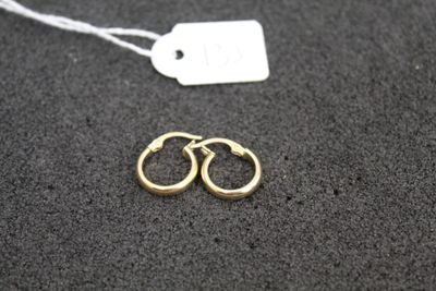 two pairs of gold hoop earrings on a black surface with a price tag