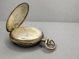 a silver pocket watch sitting on a table with a key