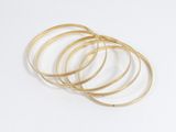 une pile de bracelets « bangies » dorés sur fond blanc