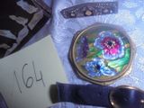 un petit miroir orné d'une fleur, à côté d'une cuillère et d'un repose-cuillère