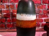 un vase noir et marron posé sur une table devant un mur de briques