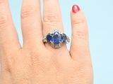 an image of a woman ' s hand holding a blue sapphire and diamond ring