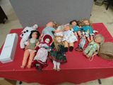 a lot of dolls sitting on a table with a red table cloth