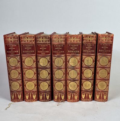 six livres rouges ornés de médaillons dorés sont alignés sur une surface blanche