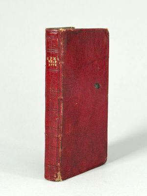 un vieux livre rouge posé sur une table à côté d'un mur blanc