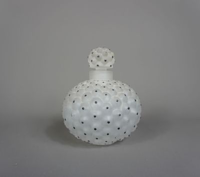 un vase blanc parsemé de points noirs, posé sur une surface grise
