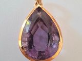 un gros plan d'un pendentif en pierre violette posé sur une surface blanche