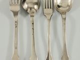 quatre cuillères en argent et une fourchette sont alignées sur une surface blanche