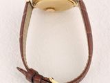 a close up of a watch on a white surface with a brown strap