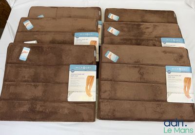 quatre tapis de bain marron portant des étiquettes, posés sur un lit