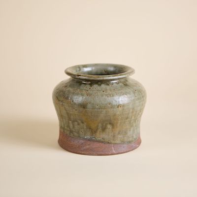 un petit vase vert avec un socle marron sur un fond blanc