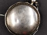 an antique silver pocket watch on a chain on a black surface