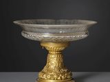 un bol en verre ancien posé sur un socle doré, sur fond noir