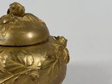 gold plated teapot with lid and leaf decoration on a white surface